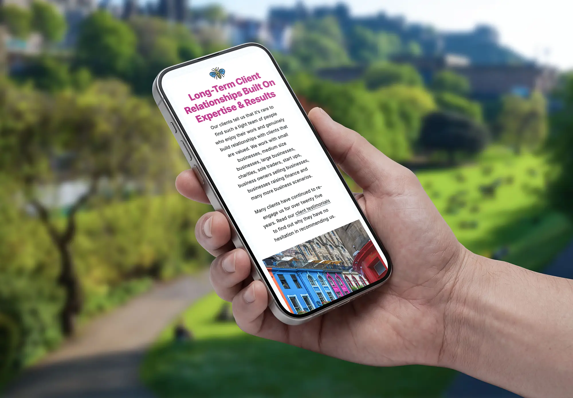 Hand holding a smartphone displaying the Johnston Smillie website against a green park backdrop